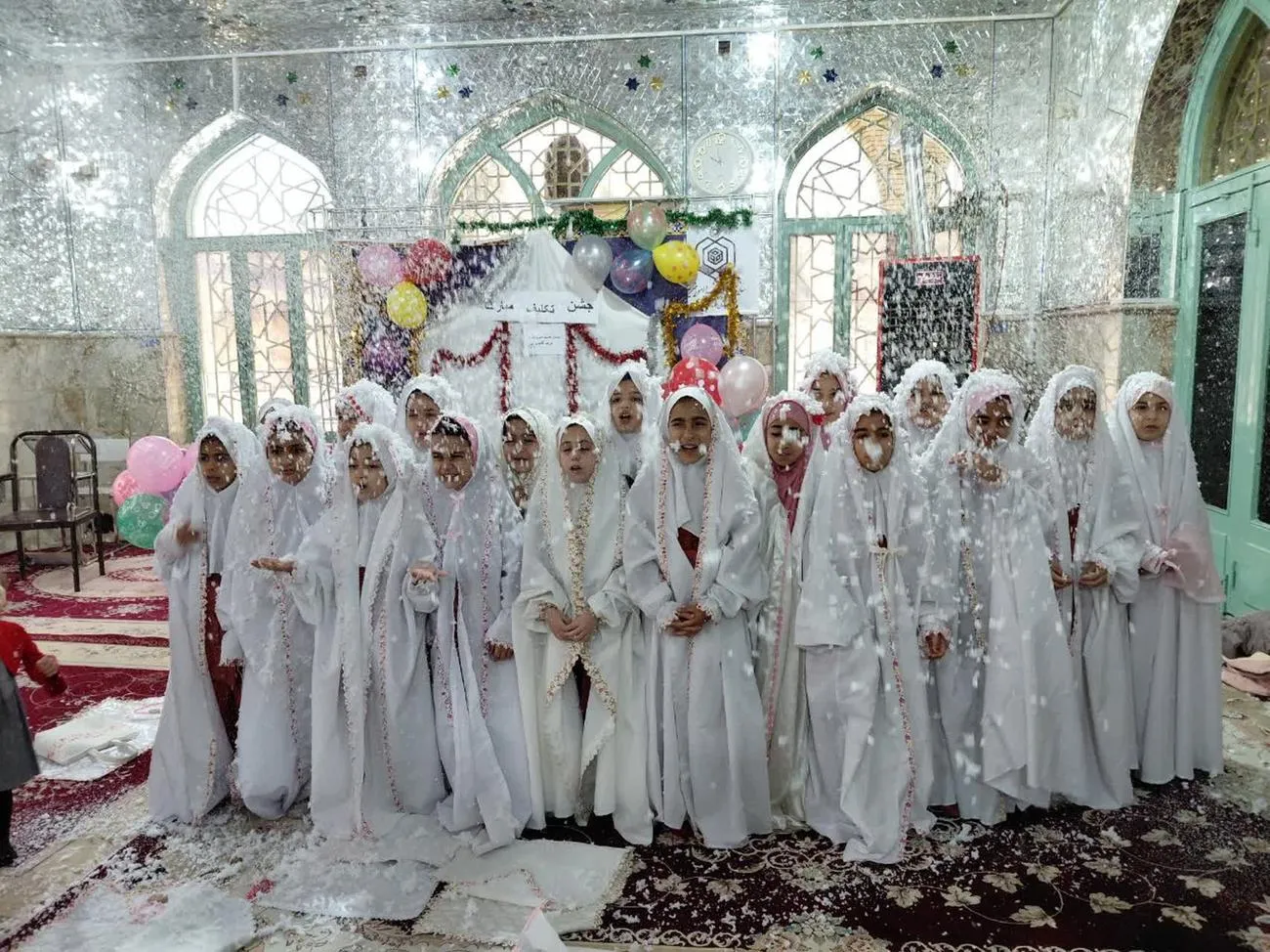 تصویری از مراسم جشن تکلیف دانش‌آموزان دختر بخش درب‌گنبد با چادرهای سفید در صحن امامزاده محمد(ع) شهرستان کوهدشت