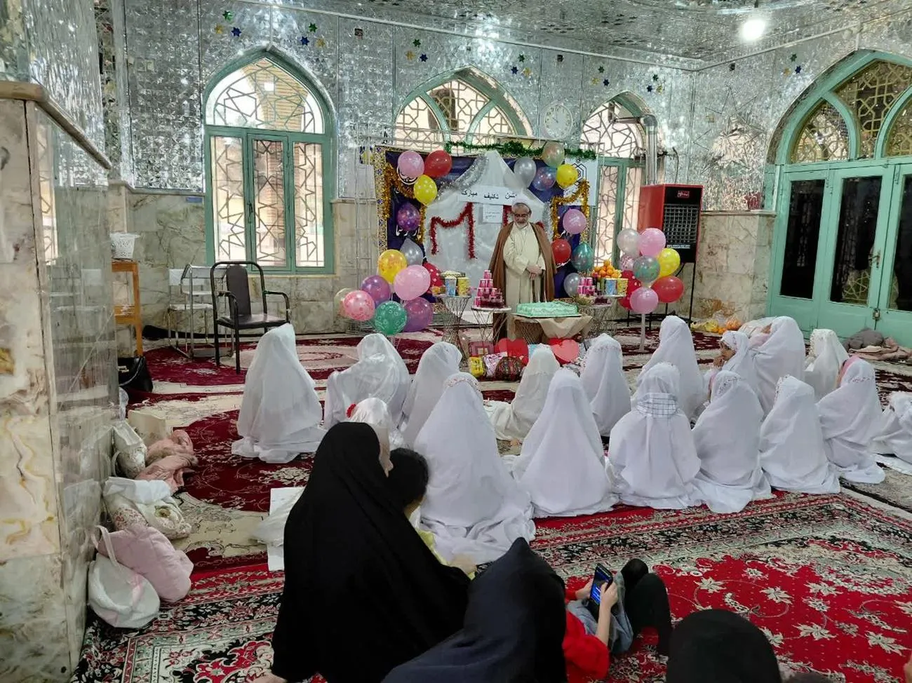 تصویری از مراسم جشن تکلیف دانشآموزان دختر بخش دربگنبد با چادرهای سفید در صحن امامزاده محمد(ع) شهرستان کوهدشت