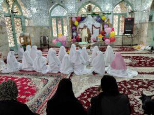 تصویری از مراسم جشن تکلیف دانش‌آموزان دختر بخش درب‌گنبد با چادرهای سفید در صحن امامزاده محمد(ع) شهرستان کوهدشت