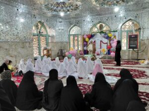تصویری از مراسم جشن تکلیف دانش‌آموزان دختر بخش درب‌گنبد با چادرهای سفید در صحن امامزاده محمد(ع) شهرستان کوهدشت