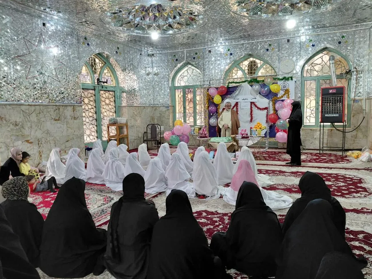 تصویری از مراسم جشن تکلیف دانشآموزان دختر بخش دربگنبد با چادرهای سفید در صحن امامزاده محمد(ع) شهرستان کوهدشت